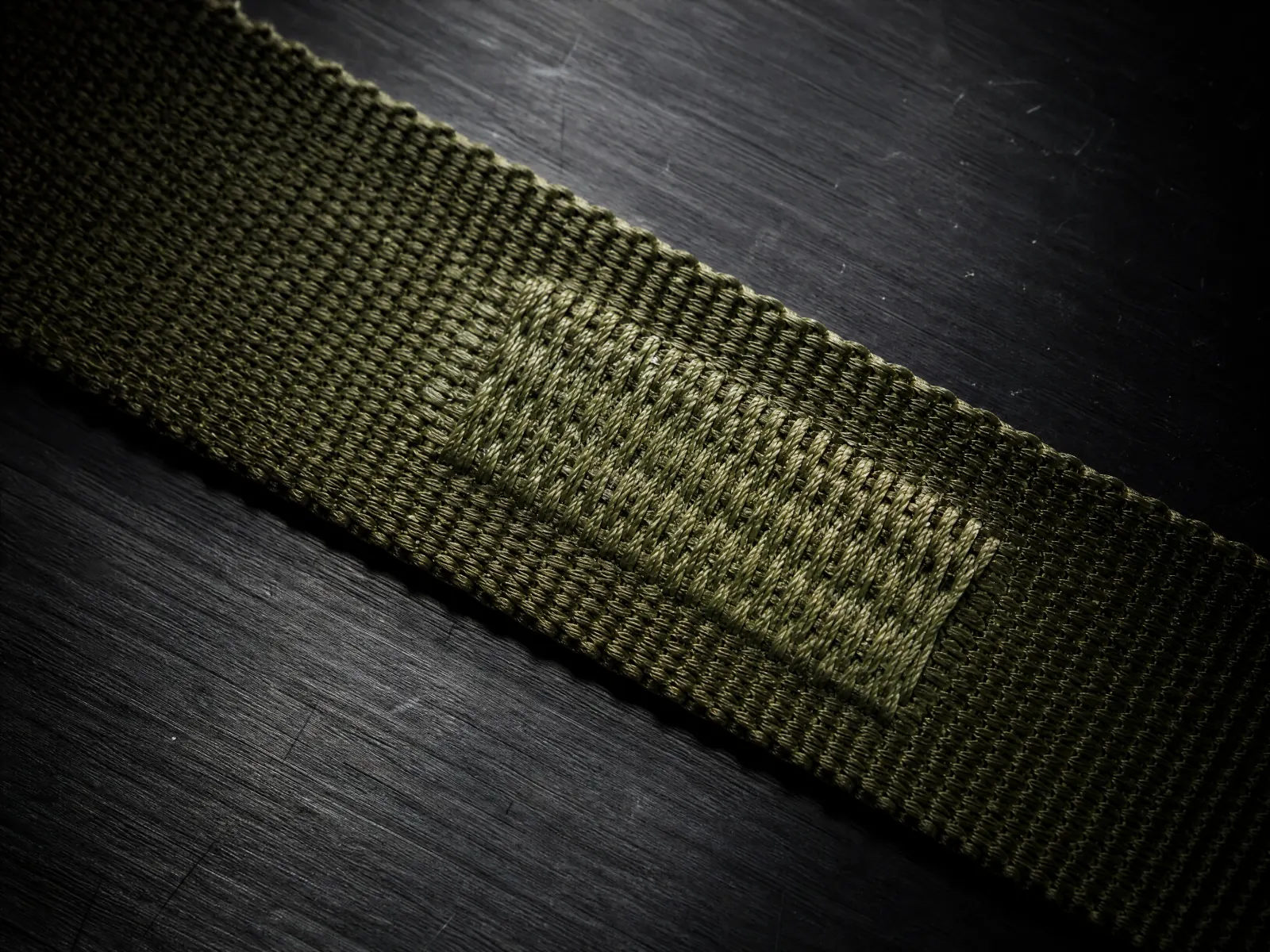 Macro of a bar-tack stitched in olive thread across flat woven webbing